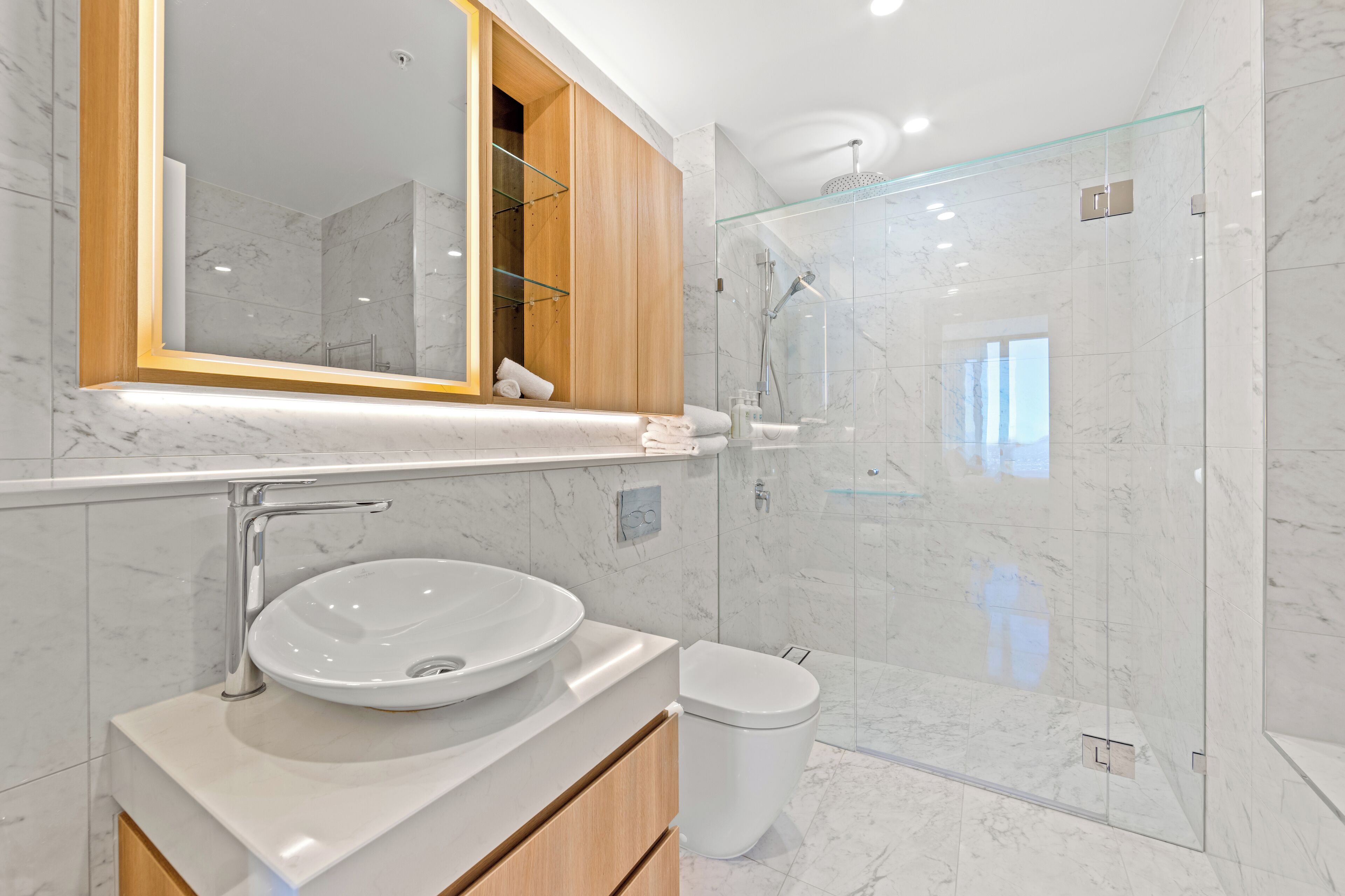 A modern bathroom with a marble sink, a glass-enclosed shower, and a wooden vanity.