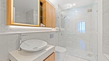A modern bathroom with a marble sink, a glass-enclosed shower, and a wooden vanity.
