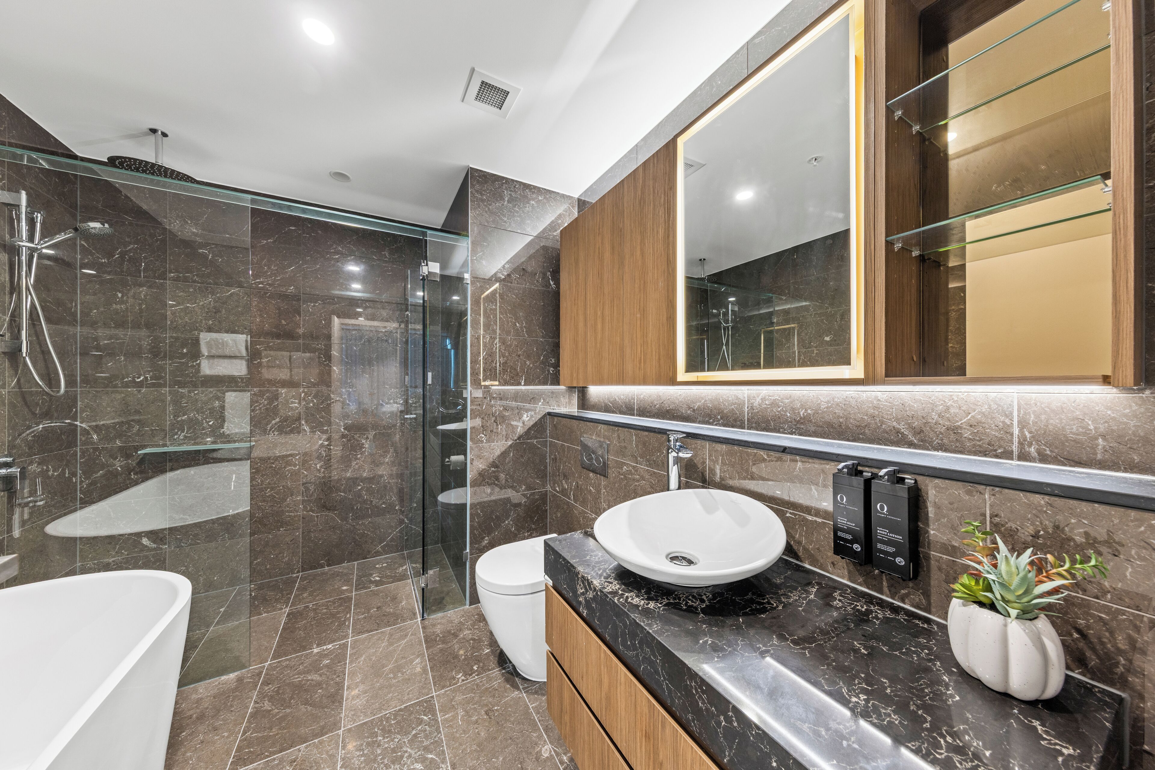 Un baño moderno con cabina de ducha de vidrio, un lavabo blanco y suelo de baldosas de mármol.