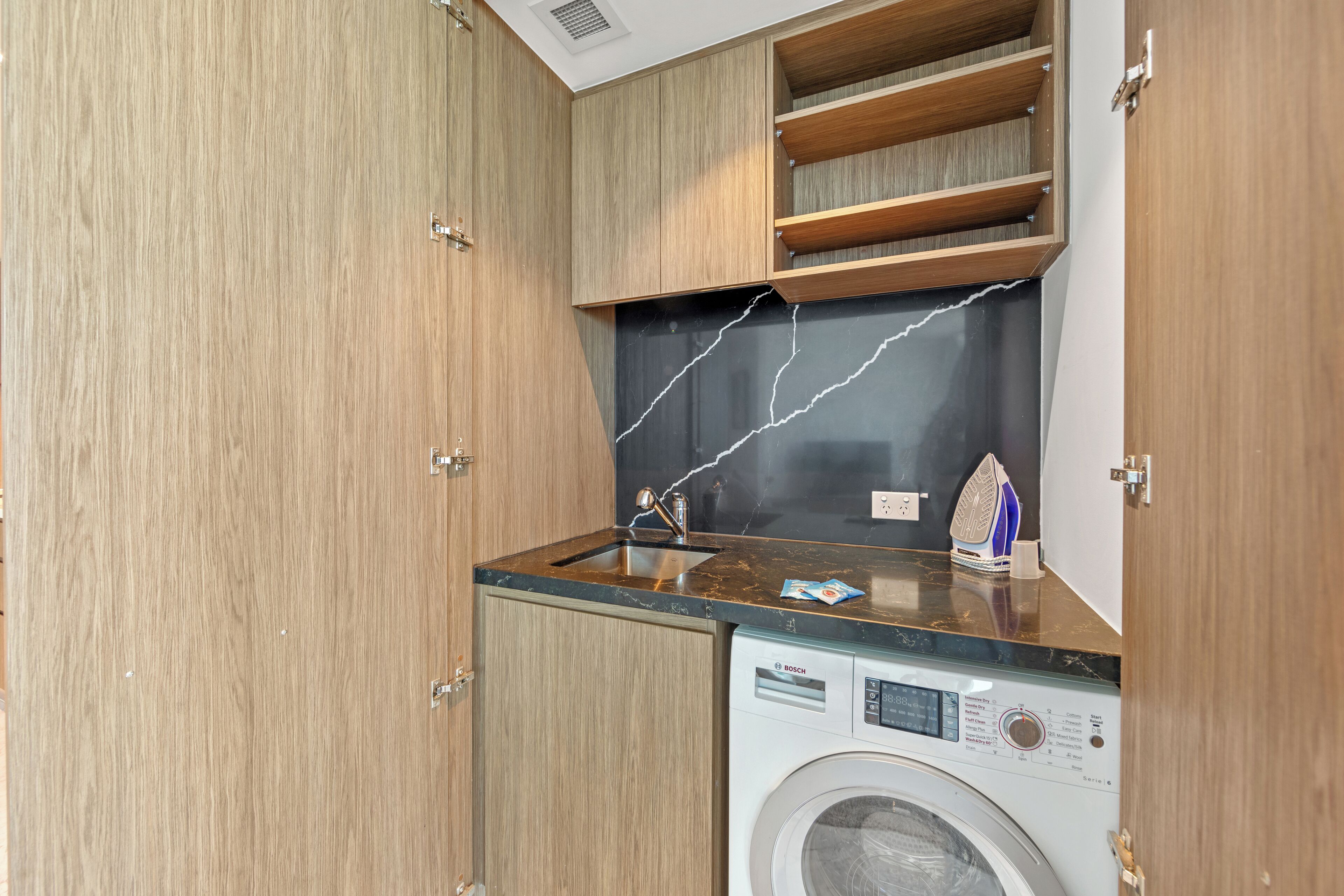 Een compacte keuken met houten kastjes, een ingebouwd spoelgedeelte en een Bosch wasmachine.