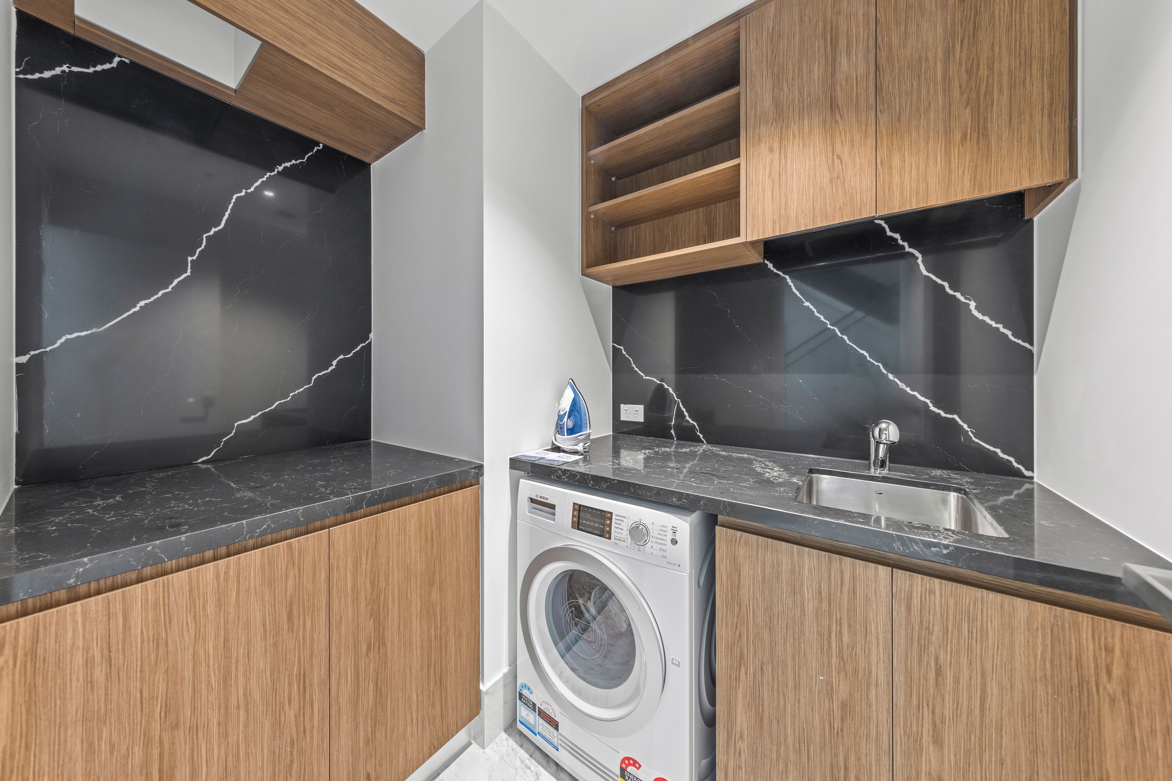 A modern kitchen with a built-in washer, wooden cabinets, and black marble countertops.