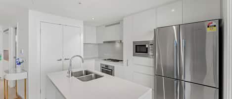 A modern kitchen with white cabinetry, stainless steel appliances, and a central island with a sink.