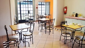 A dining area with multiple tables and chairs, a fire extinguisher mounted on the wall, and a checkered tablecloth on one table. - Horizon Inn (Harare)
