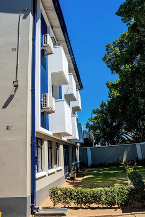 A modern building with a flat facade, multiple balconies, and a well-maintained lawn.