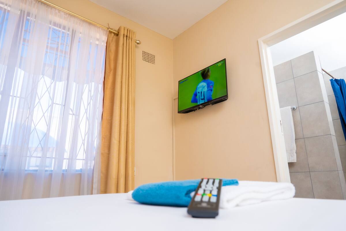 Une chambre d’hôtel avec un lit, une télécommande et un téléviseur fixé au mur.
