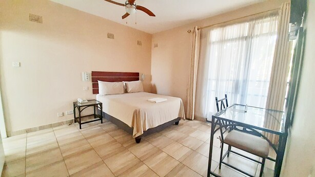A hotel room with a bed, bedside table, and a glass table with chairs. - Horizon Inn (Harare)