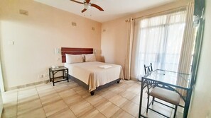 A hotel room with a bed, bedside table, and a glass table with chairs. - Horizon Inn (Harare)