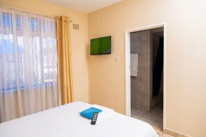 A hotel room with a bed, a remote control, a television on the wall, and a bathroom door.