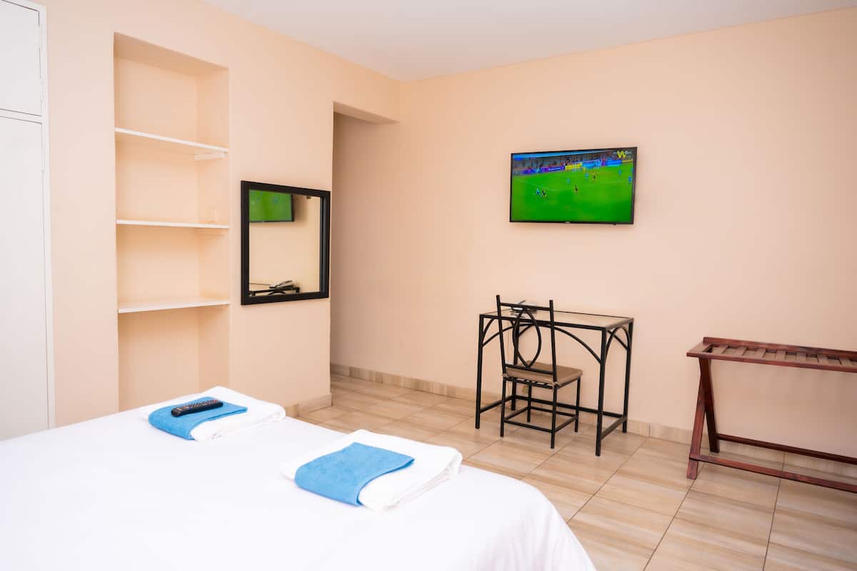 Une chambre d’hôtel avec deux lits, un bureau, une chaise, une télévision et une étagère.