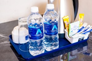 Una bandeja con dos botellas de agua Aquaclear, un vaso, una cafetera y un dispensador de snacks.