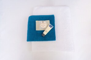 A white towel and a blue towel with a bar of soap and a bar of body lotion on top.