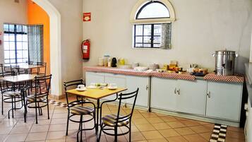 Un comedor con mesas y sillas, un extintor, una ventana y una encimera de cocina con diversos objetos.