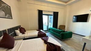A hotel room with two beds, a green sofa, a flat-screen TV, and a balcony with curtains. - Wb Weekend Otel  (Bodrum)