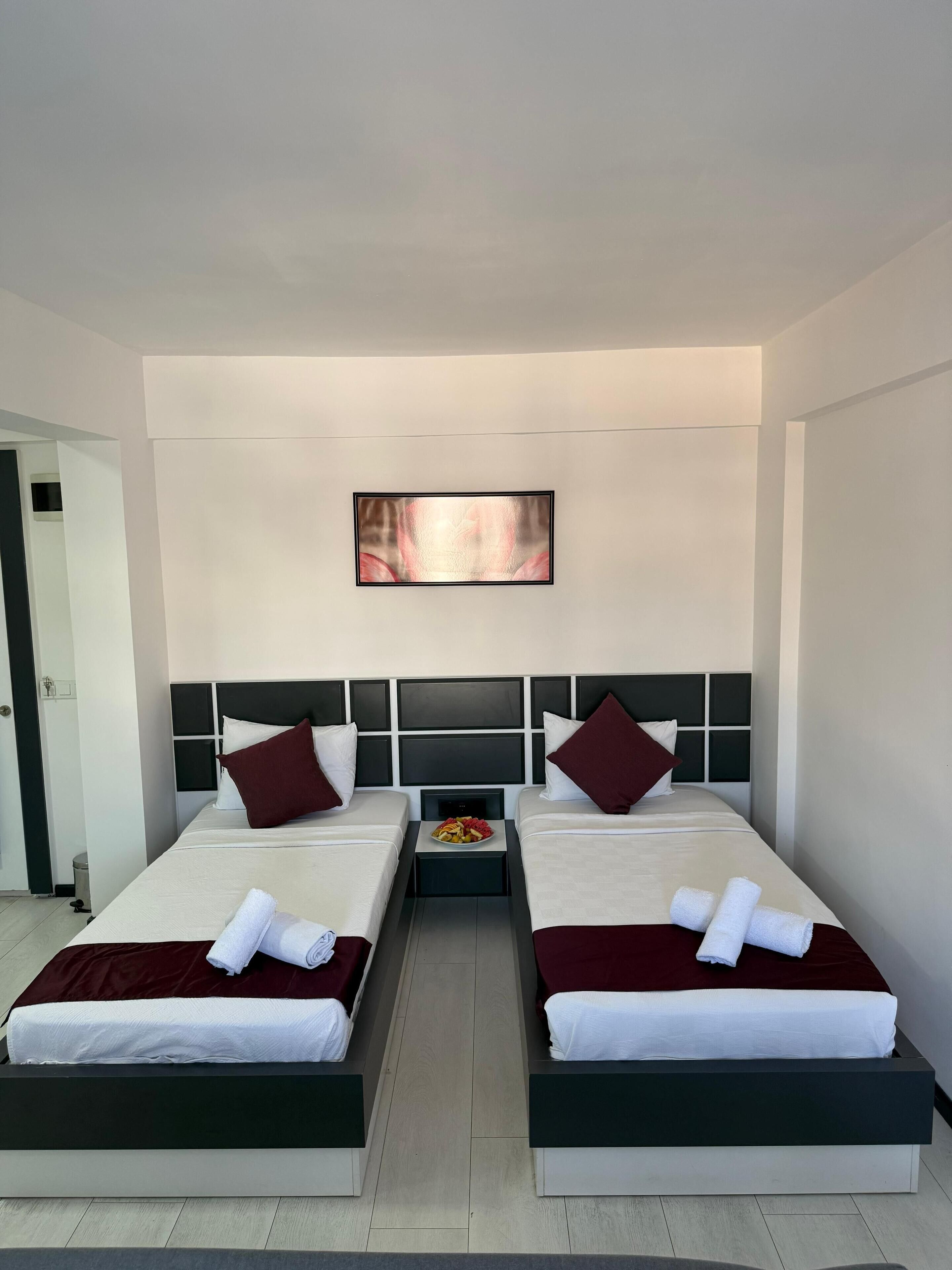 Una habitación de hotel con dos camas, una mesita con fruta y un cuadro en la pared.
