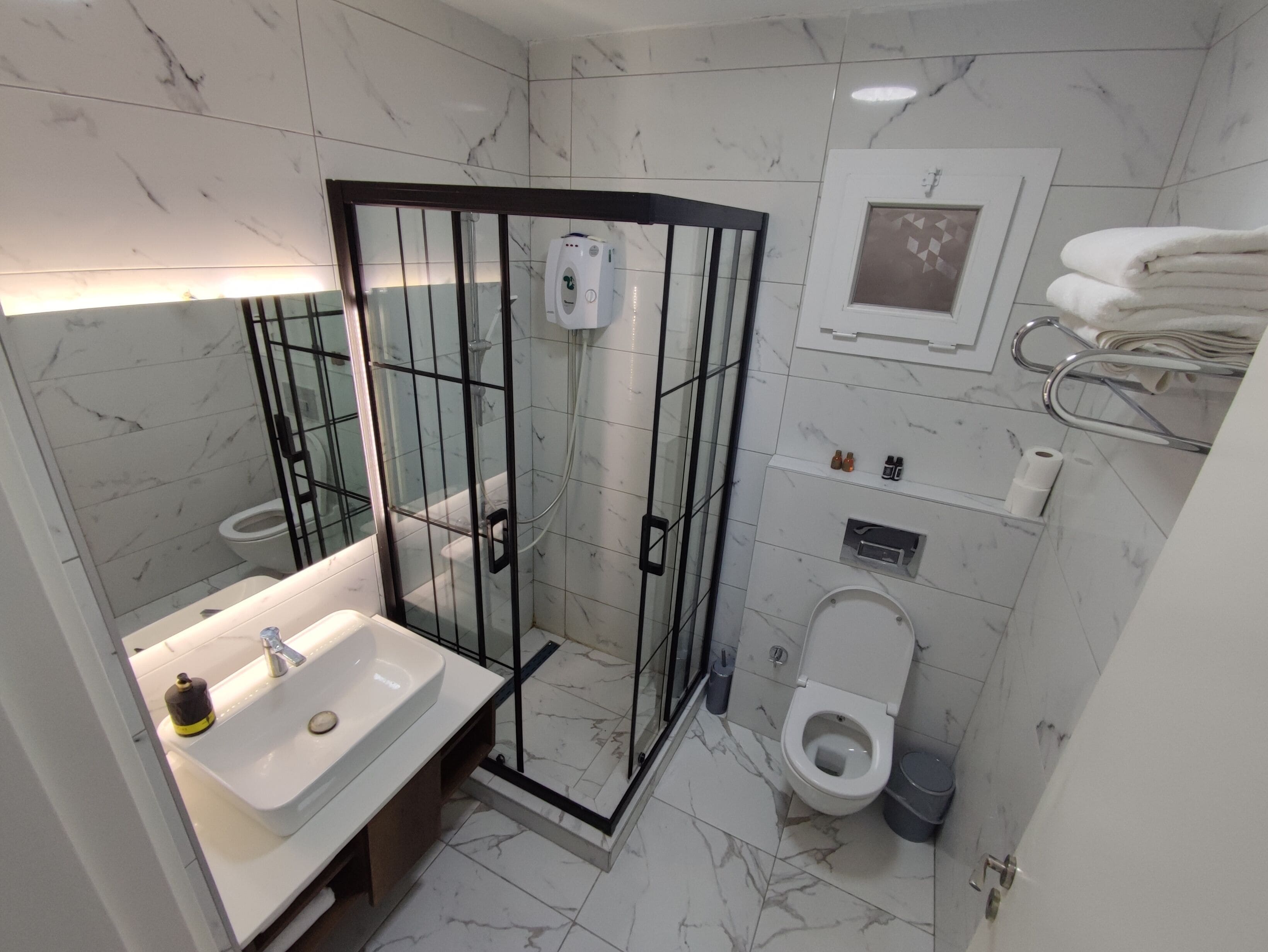 Un baño con ducha envuelta en vidrio, un lavamanos con dispensador de jabón, un inodoro y un perchero para toallas.
