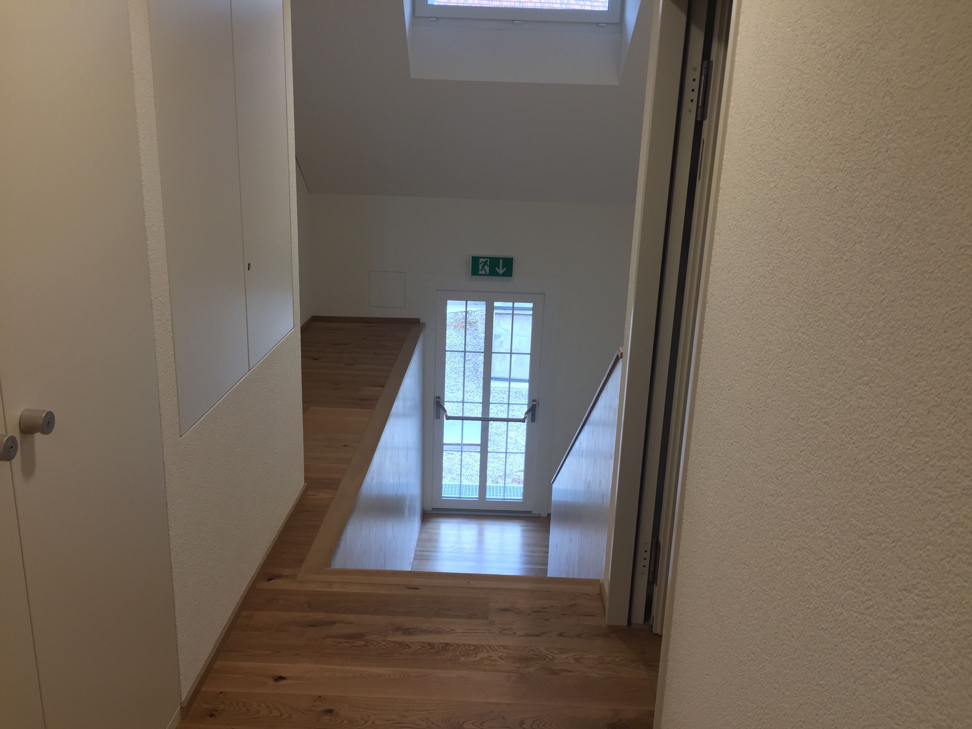 A narrow, wooden-floored corridor with a door on the left and a window at the end.