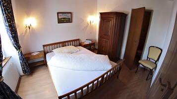 A bedroom with a bed, a wooden wardrobe, a chair, and two wall-mounted lamps.