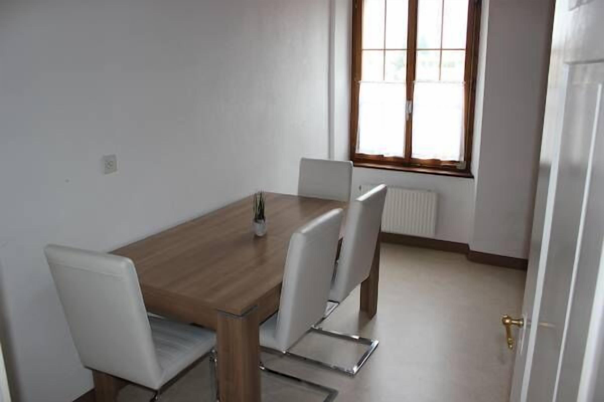 A dining area with a wooden table and four chairs, a window with blinds, and a radiator.