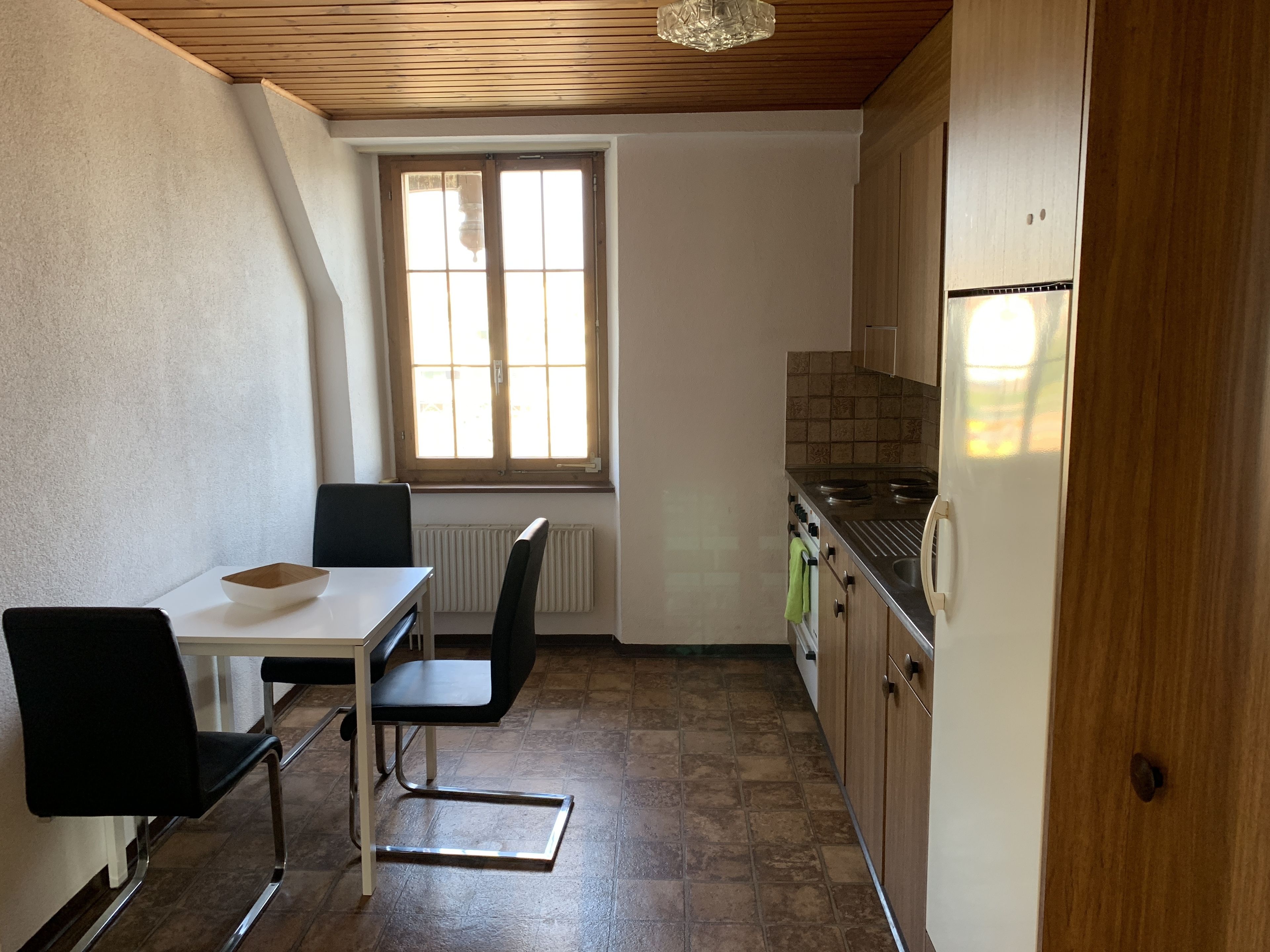 A small kitchen with a dining table and chairs, a window, and a refrigerator.