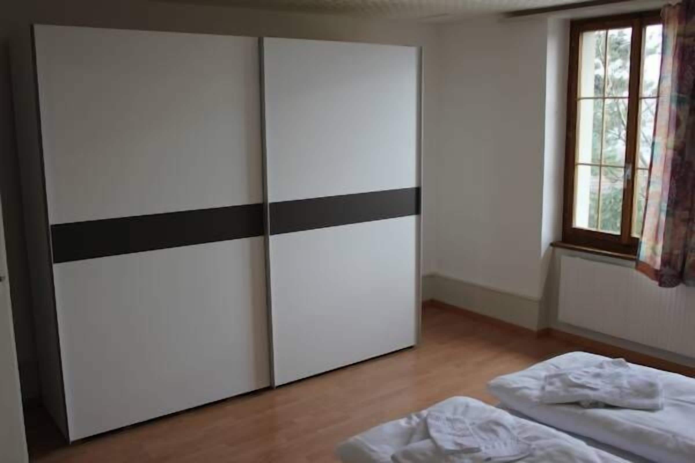 Una habitación con armario, una ventana con cortinas y una cama con ropa blanca de cama.