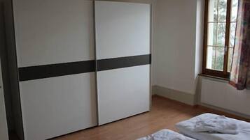 Una habitación con armario, una ventana con cortinas y una cama con ropa blanca de cama.