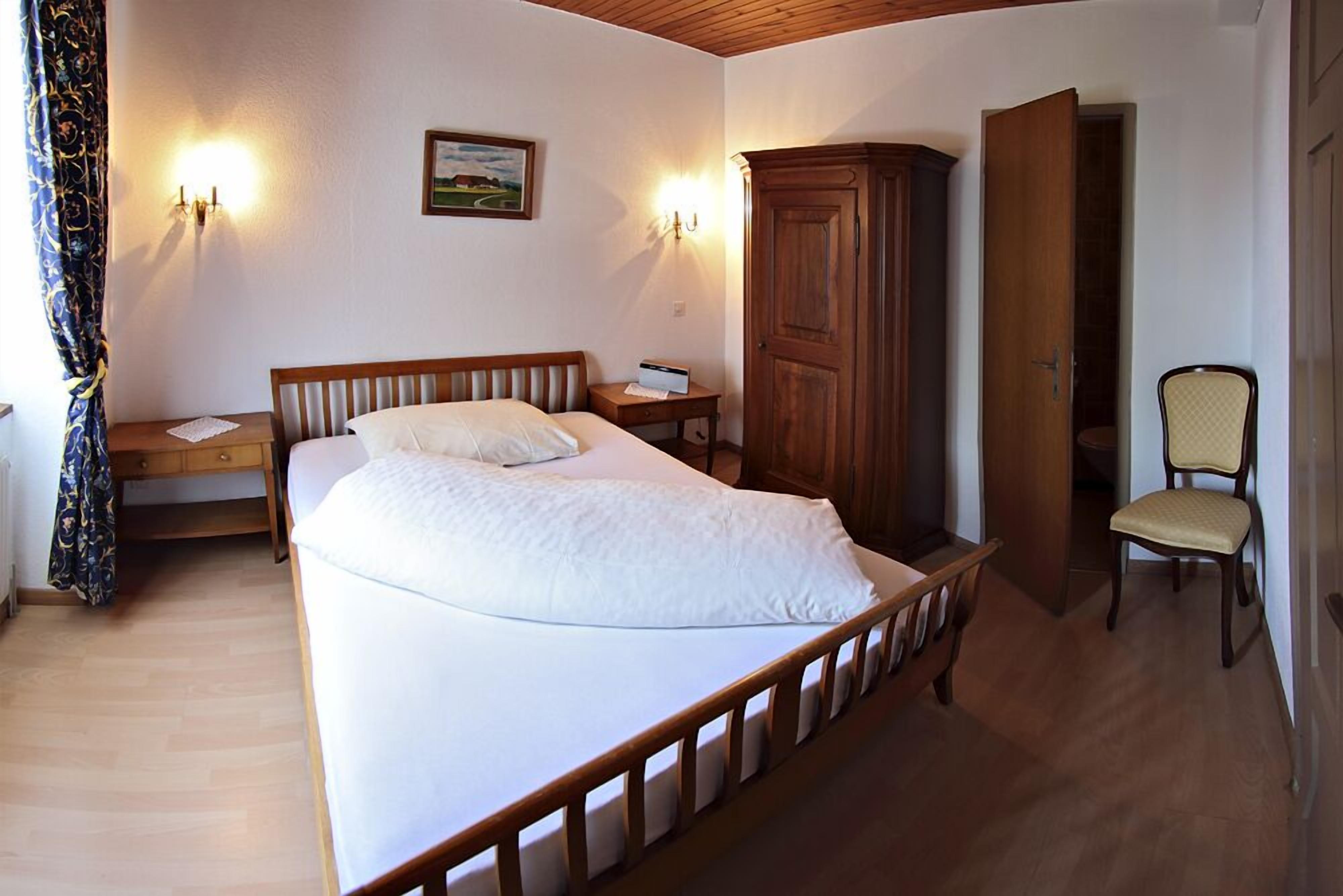 Een slaapkamer met een houten bed, nachtkastje, kledingkast en stoel.