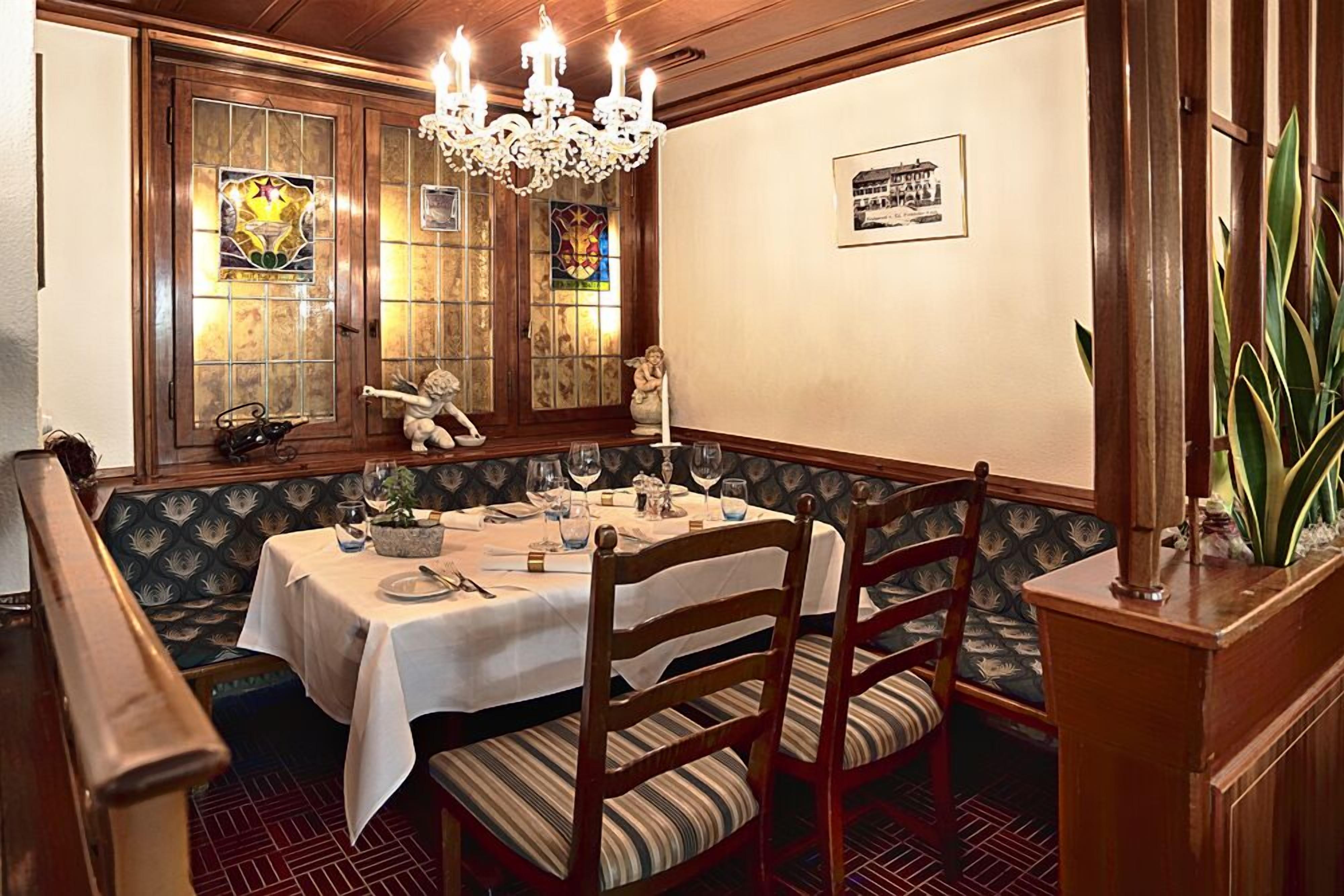 Un comedor con disposición de asientos tipo cabina, una araña y un vitral.