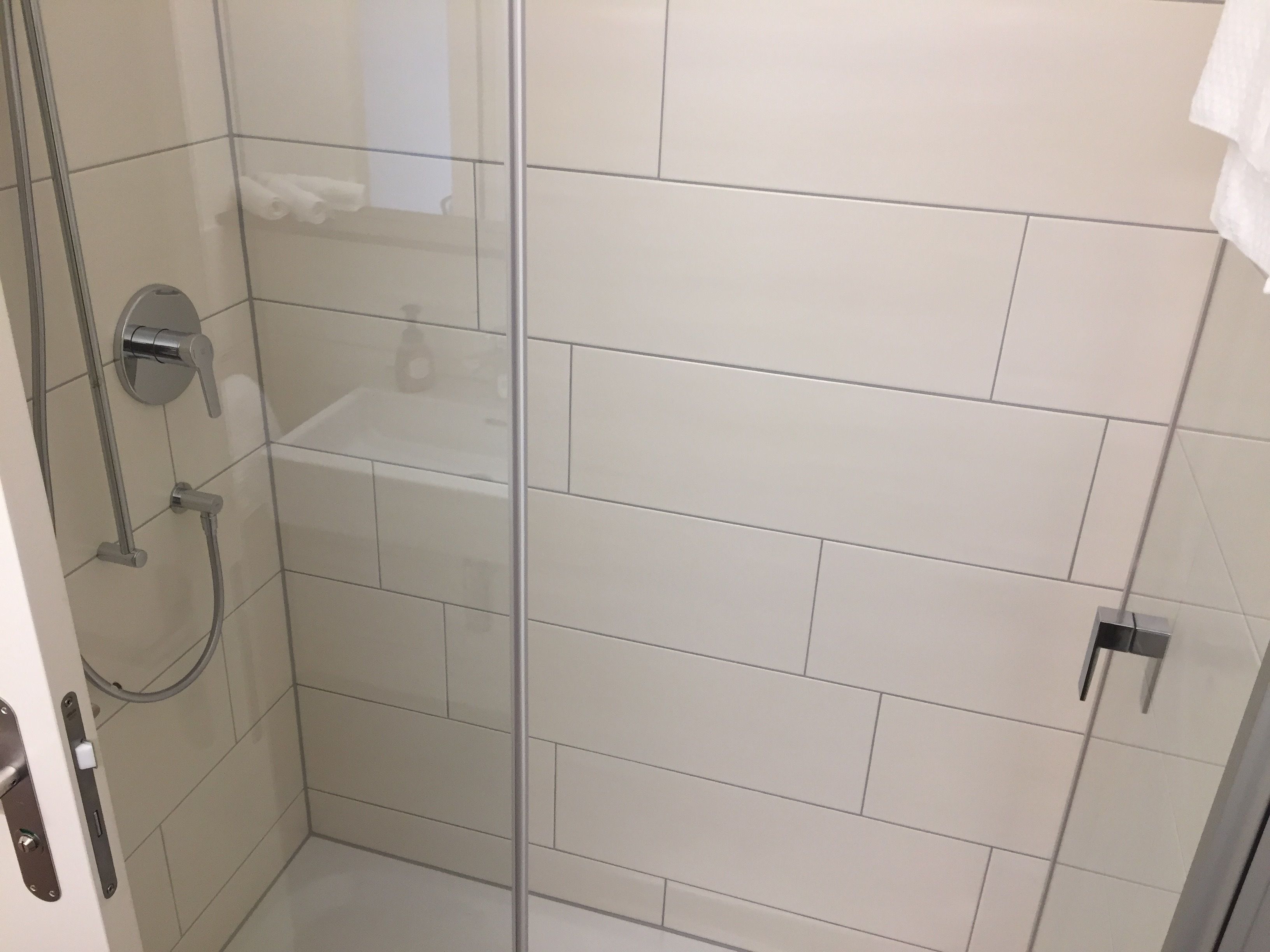 Ein modernes Badezimmer mit weißen Fliesen, einer Duschkabine aus Glas und einem sichtbaren Toilettenpapierhalter.