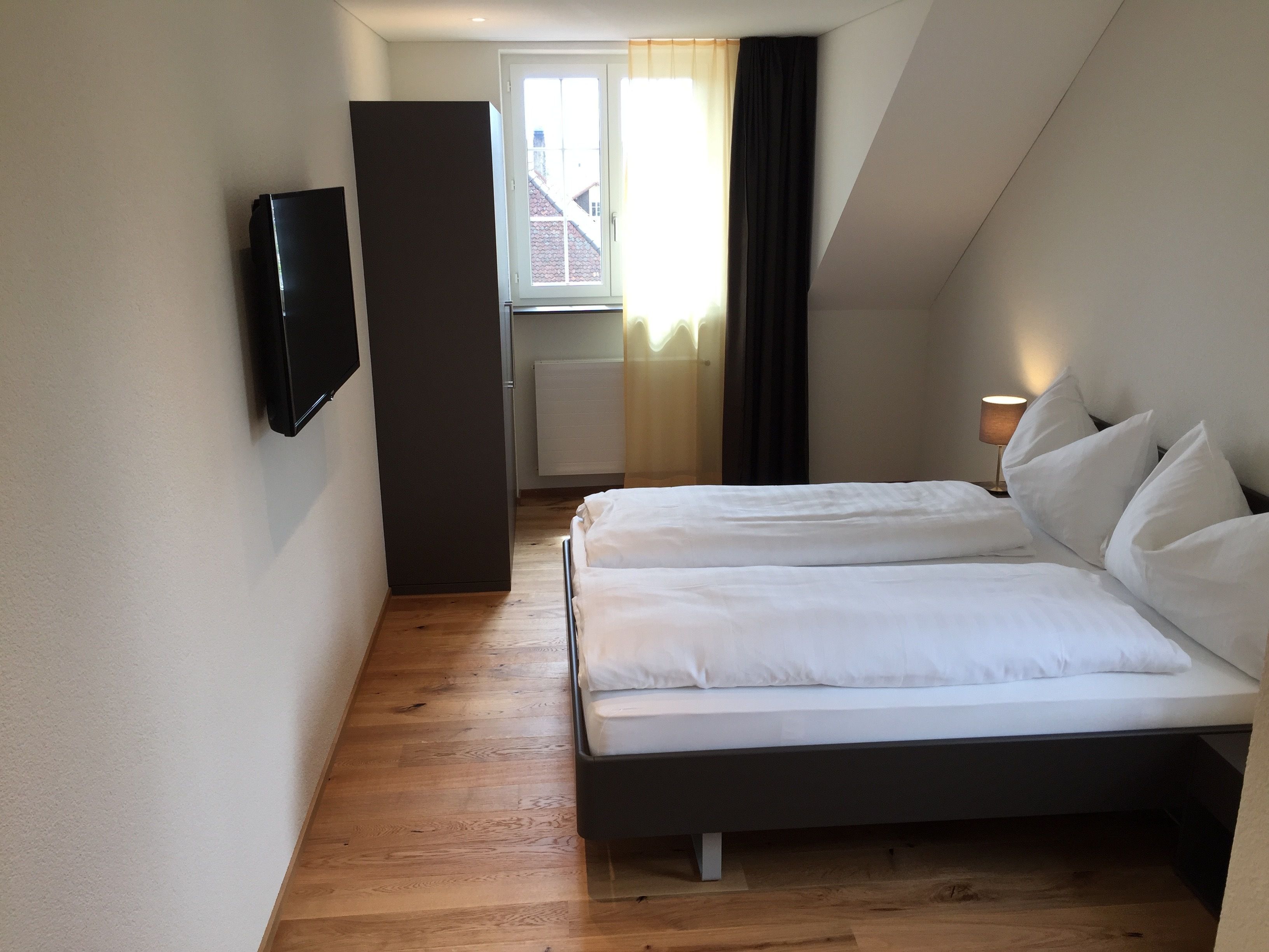 Una habitación de hotel moderna con una cama, un televisor de pantalla plana y una ventana con cortinas.