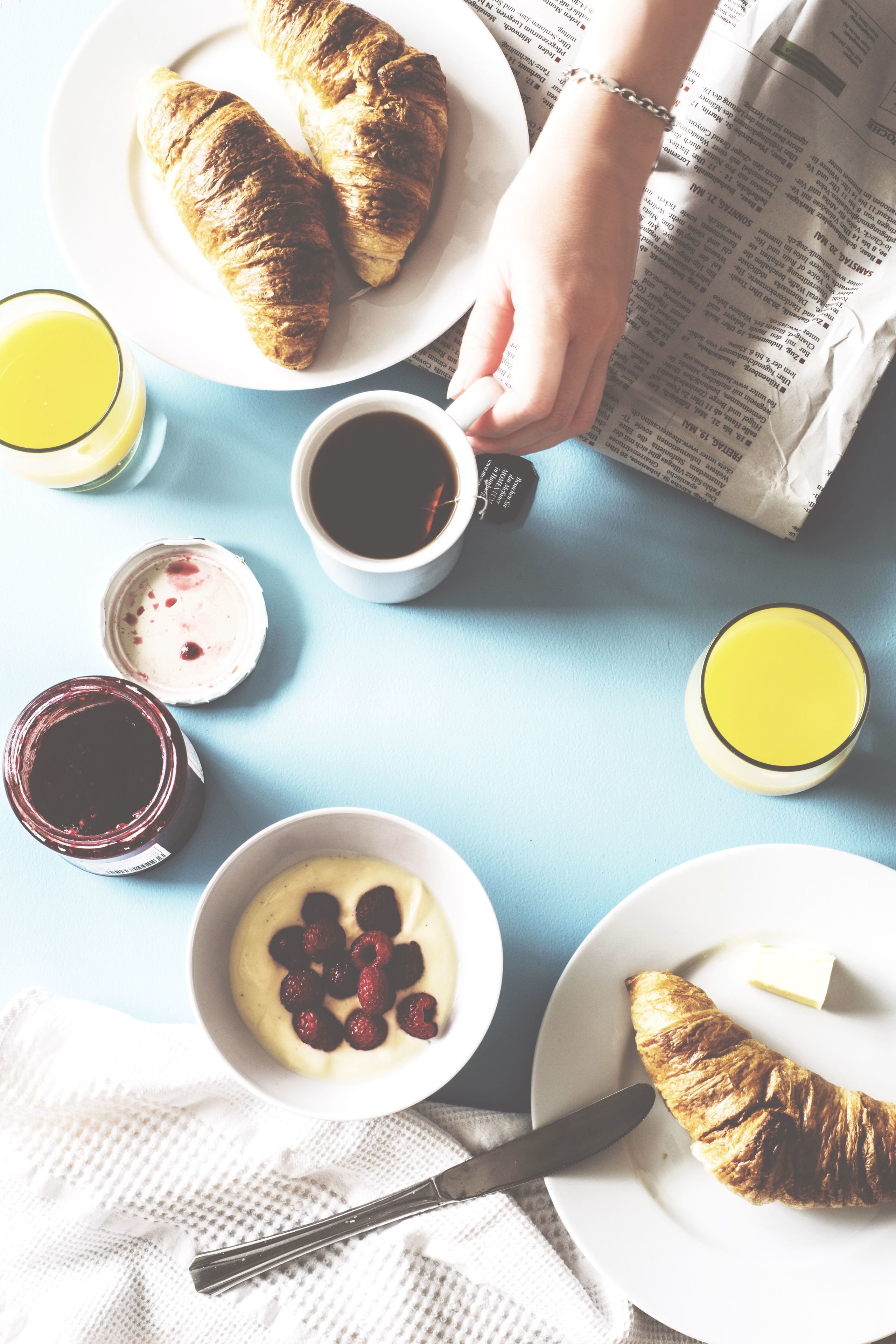 Un desayuno con cruasanes, café y un periódico sobre una mesa azul.