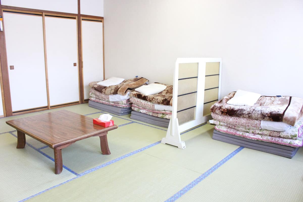 Perinteinen japanilainen huone, jossa on tatamimatto, matala puupöytä ja futon-patjat peittoineen.