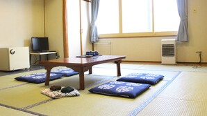 A traditional Japanese room with tatami flooring, a low wooden table, cushions, a television, and an air conditioning unit. - Biei Guest House Sirogane no Yu - Hostel (Biei)