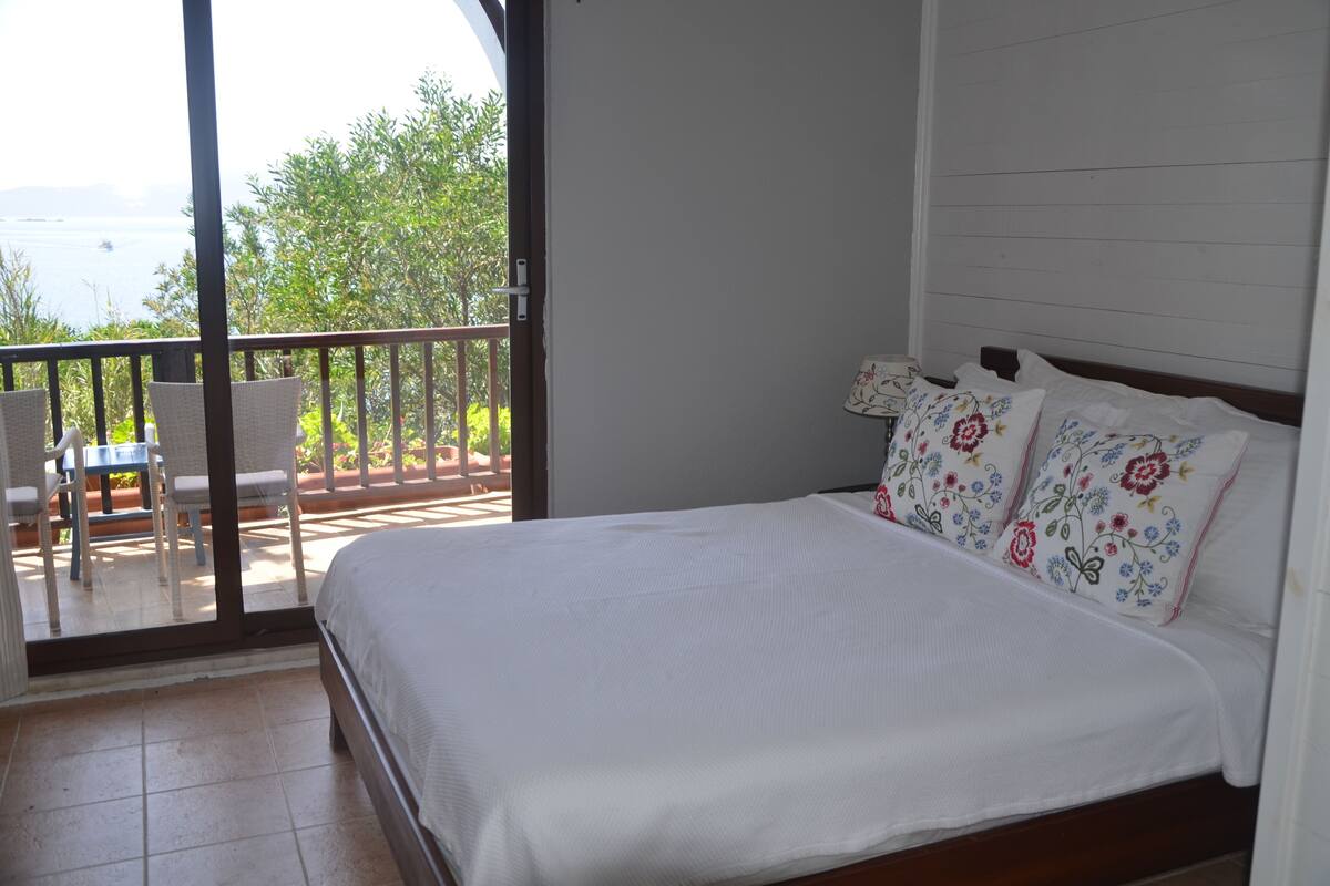 Een slaapkamer met een bed, een balkon met stoelen en uitzicht op zee.