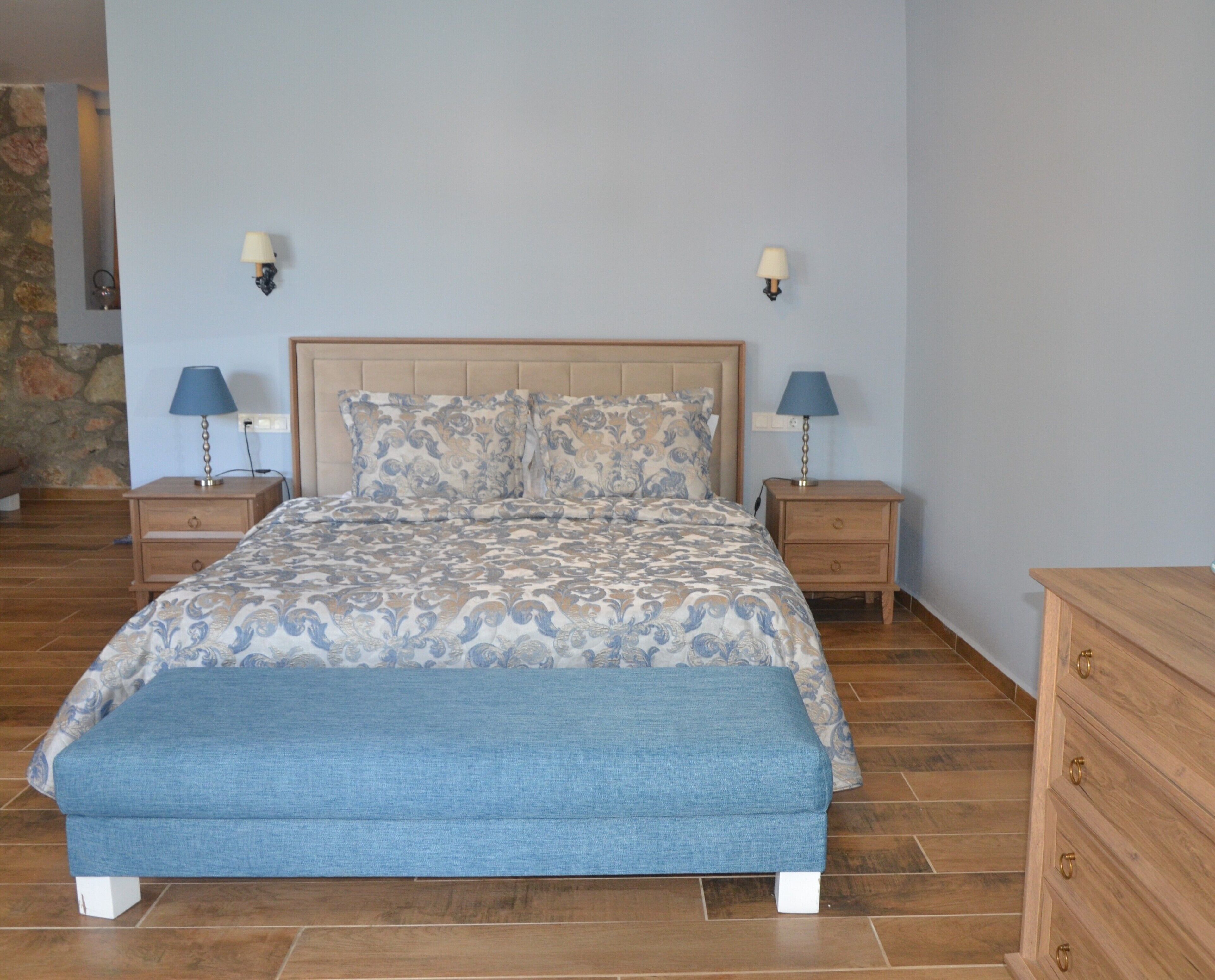Un dormitorio con una cama, dos mesitas de noche, un banco y un aparador.