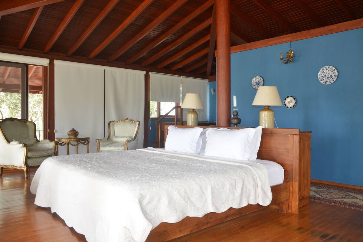 Een slaapkamer met een houten bed, twee stoelen, een kleine tafel en een blauwe muur met decoratieve borden.