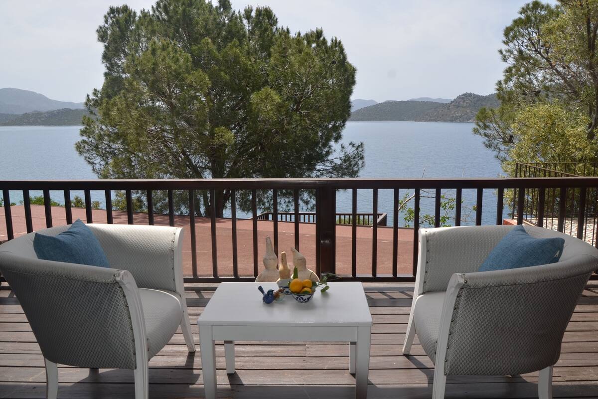 Een terras met twee stoelen en een tafel, met uitzicht op een meer en bergen op de achtergrond.