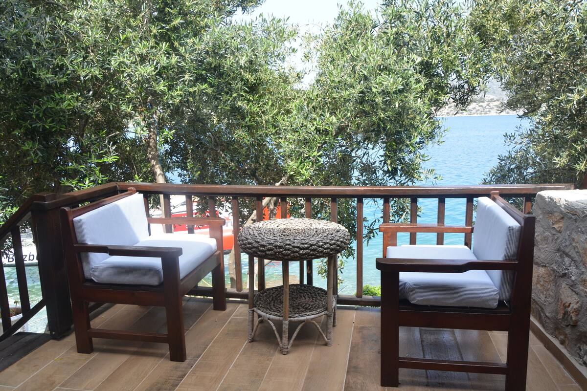 Een balkon met twee houten stoelen en een kleine ronde tafel, met uitzicht op water en groen.