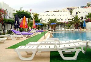 A poolside area with white lounge chairs and umbrellas, a green artificial turf, and a pool. - Hotel Baba (Bodrum)
