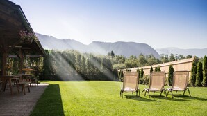 Un patio con tavoli e sedie di legno, un'area salotto coperta e una vista sulle montagne sullo sfondo.