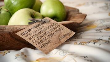 A wooden bowl with green apples on a bed with a floral pattern.