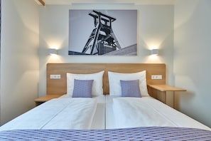 A double bed with a wooden headboard, two bedside tables, and a wall-mounted picture of a bridge. - McDreams Hotel Essen-City (Essen)