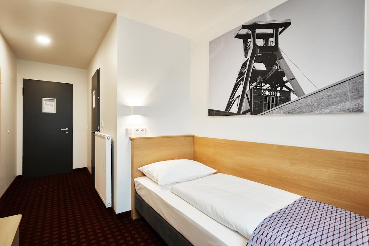 Une chambre d’hôtel avec un lit, un radiateur, une porte et une lampe fixée au mur.
