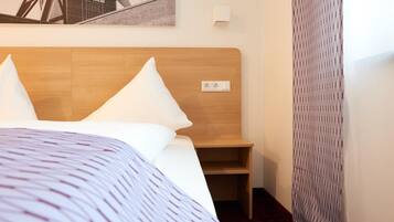 Una habitación de hotel con cabecera de madera, una cama con ropa blanca, una mesita de noche de madera y una lámpara de pared.