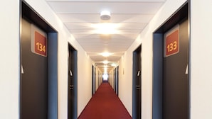 Un largo y estrecho pasillo de hotel con alfombra roja y puertas a ambos lados, con los números 134 y 133.