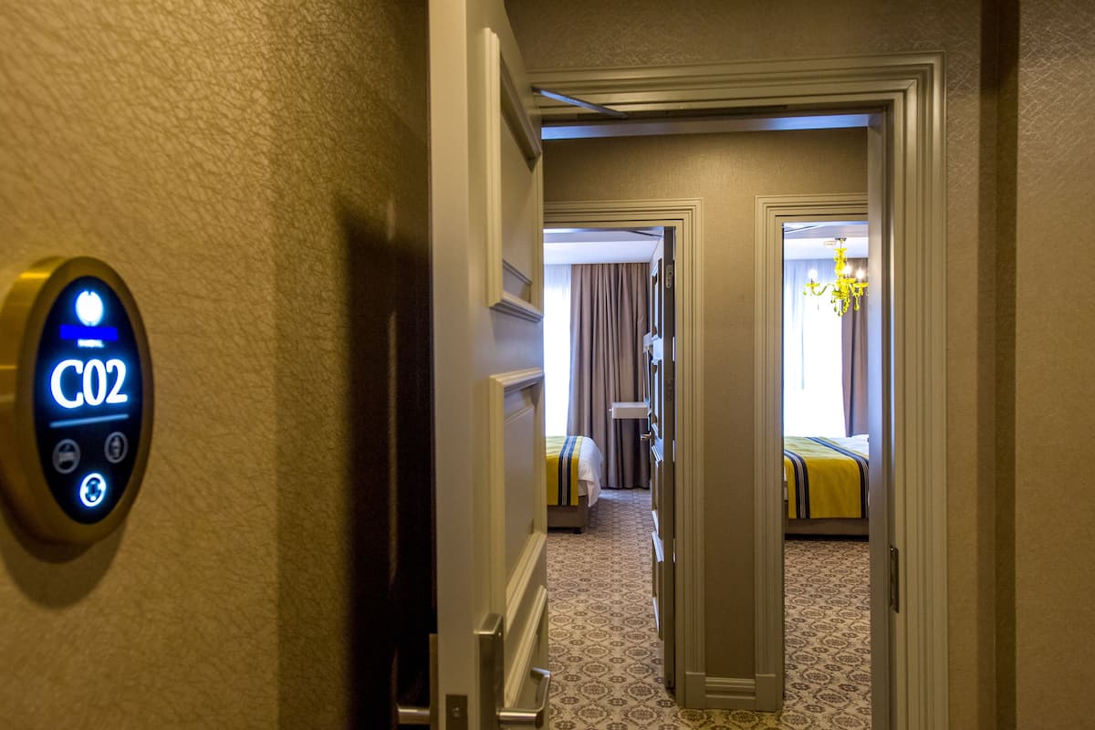 Ein Hotelgang mit einem digitalen Schlüsselescanner, einem Bett mit gestreifter Bettdecke und einem gemusterten Teppich.