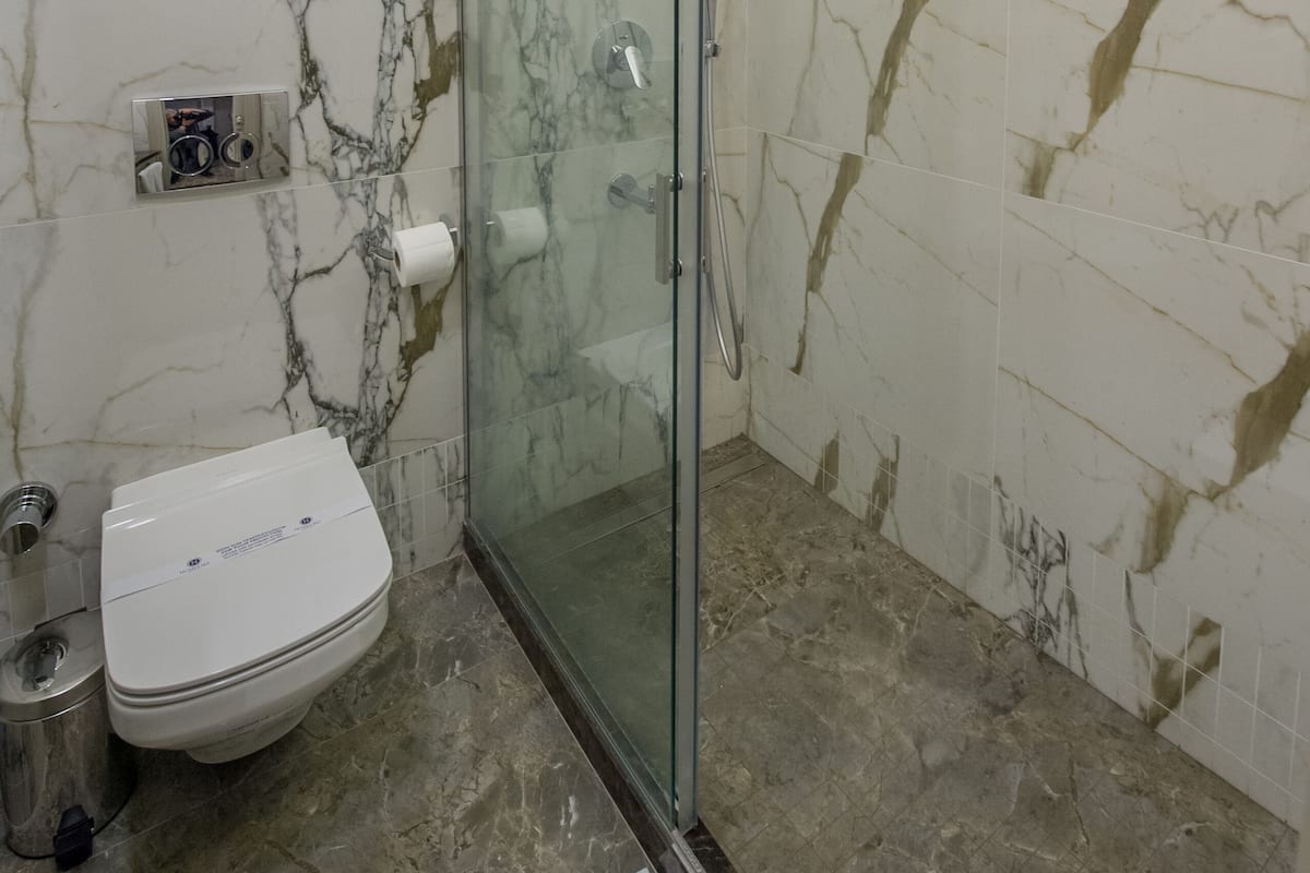 Ein Badezimmer mit einer gläsernen Duschkabine, einer Toilette und Wänden mit Marmoroptik.