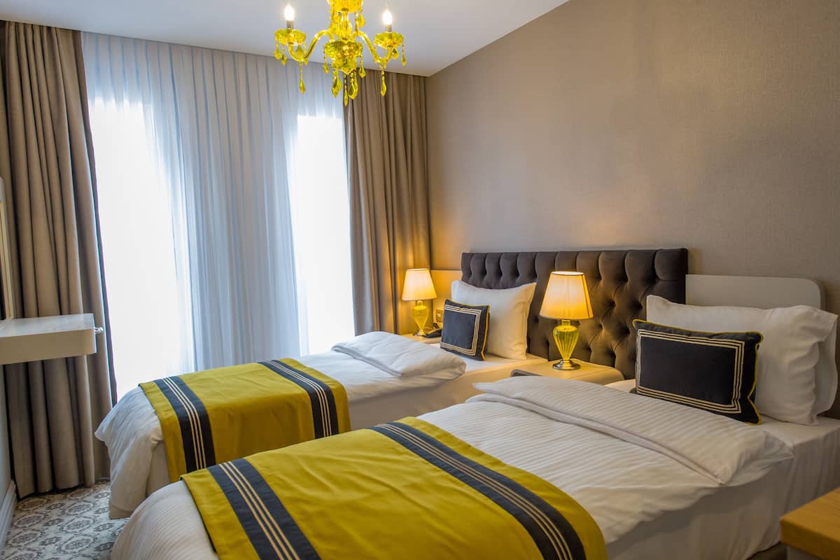 Ein Hotelzimmer mit zwei Betten, einem Kronleuchter und einem großen Fenster mit Vorhängen.