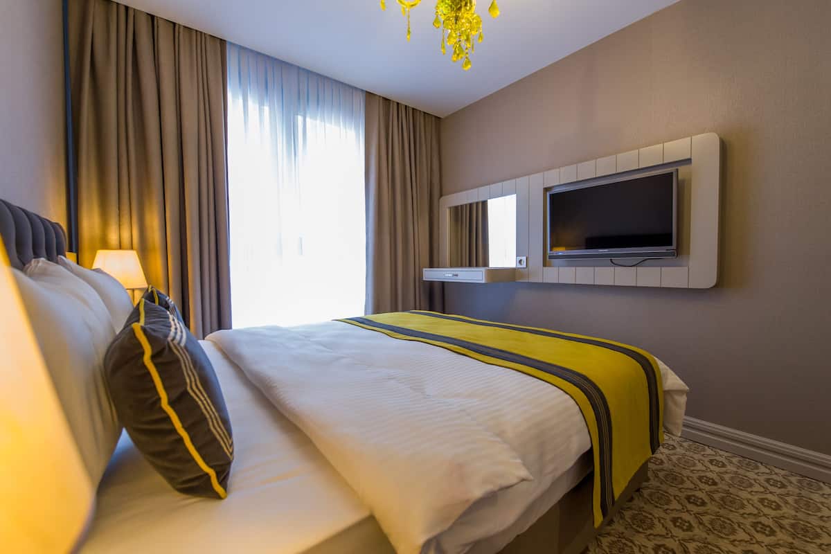 Ein Hotelzimmer mit einem Bett, einem an der Wand befestigten Fernseher und einem Fenster mit Vorhängen.