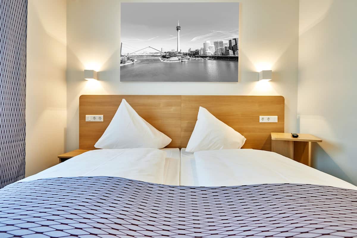 A hotel room with a bed, two bedside tables, a wall-mounted picture of a cityscape, and a patterned bedspread.