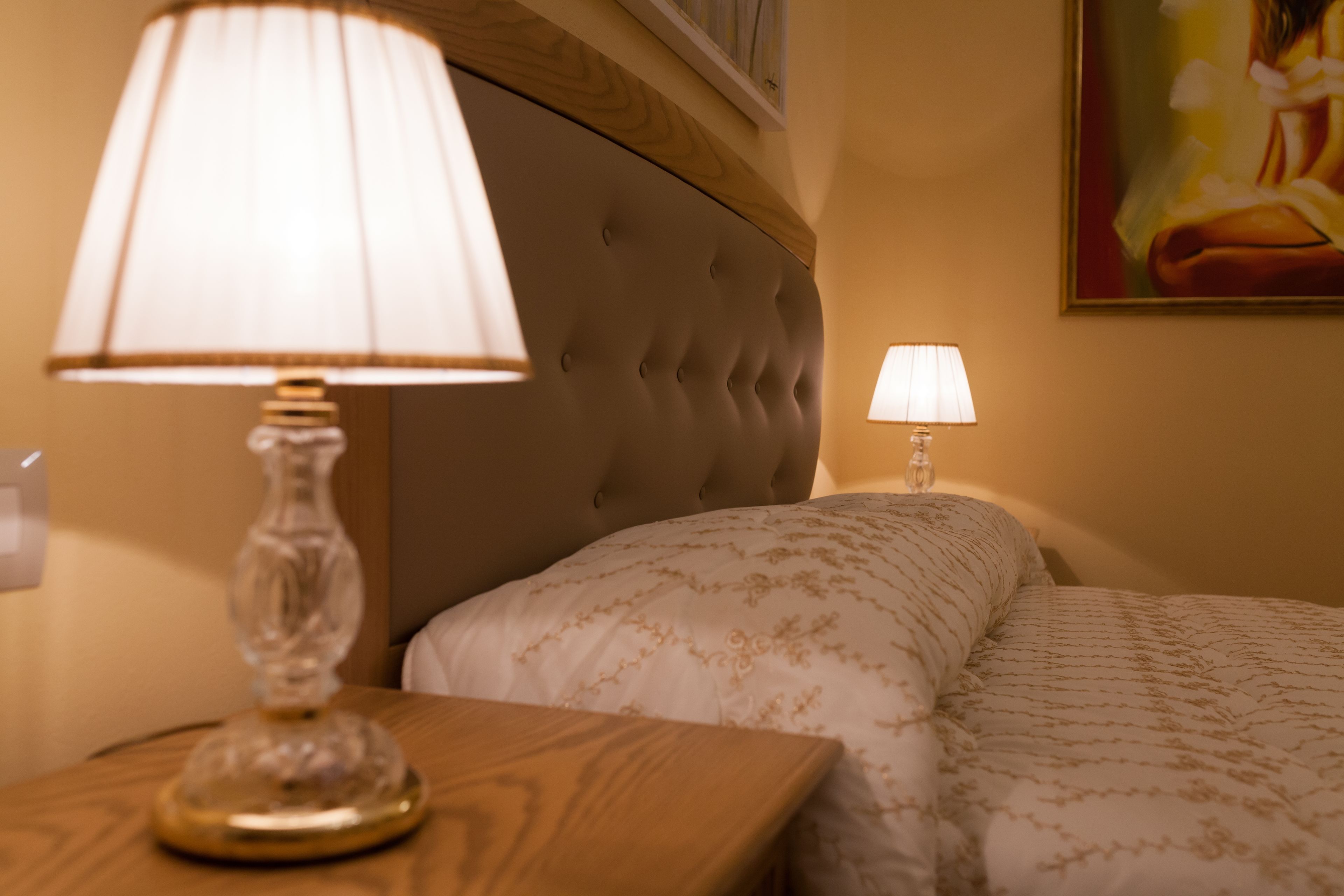 Un lit bien fait, recouvert d’une couvre-lit à motifs, avec une tête de lit capitonnée et une lampe de chevet posée sur une table de nuit en bois.